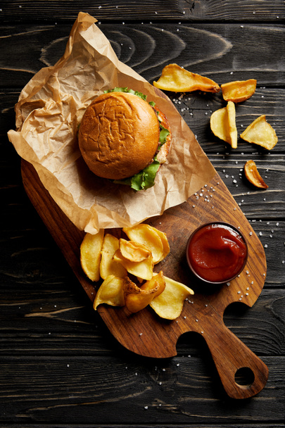 Κάτοψη του συνόλου του πρόχειρου φαγητού με burger και πατάτες σερβίρονται σε ξύλινη σανίδα - Φωτογραφία, εικόνα