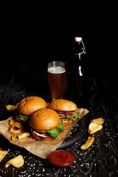 Hamburgers and french fries on table with beer in bottle and glass - Фото, зображення
