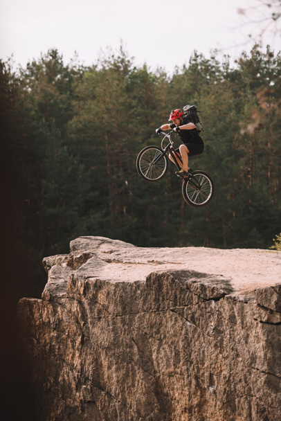 trial biker jumping on bicycle over rocky cliff outdoors - Photo, Image