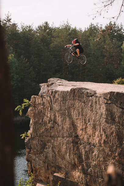 ciclista de trial saltando en bicicleta sobre acantilado rocoso al aire libre en el bosque
 - Foto, Imagen