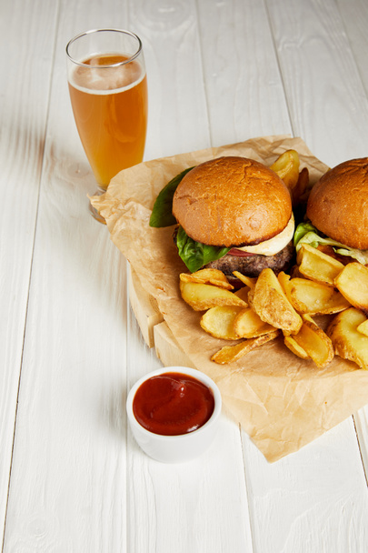 Conjunto de hamburguesas de comida chatarra y papas fritas servidas con cerveza sobre mesa blanca
 - Foto, imagen