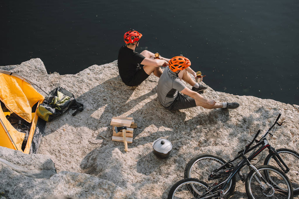 korkea kulma näkymä aktiivinen pyöräilijät syövät säilykkeitä kalliolla järven yli
 - Valokuva, kuva