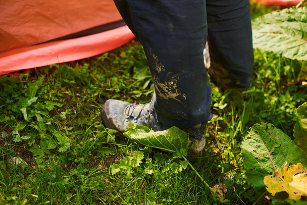 tourists put up a tent in a camping. Man's legs in dirty tourist boots next to the tent - Photo, Image