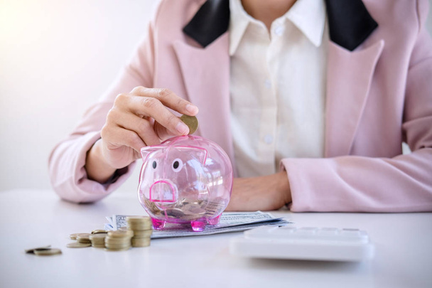 Business woman putting coins into piggy bank and using calculator to analysis business investment strategy with income of money coin and dollar, financial concept. - Foto, imagen