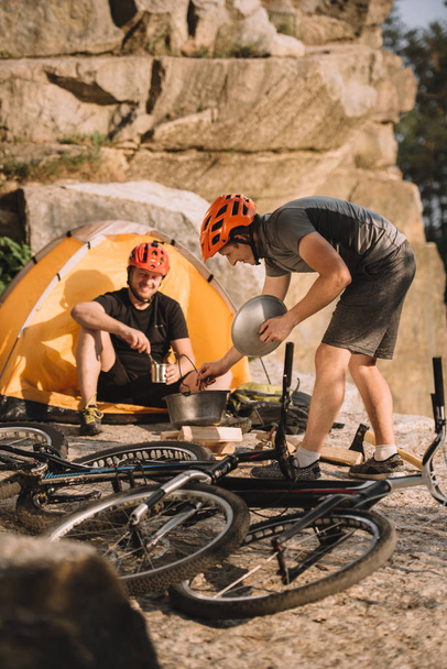 young trial bikers cooking food on camping outdoors - Photo, Image