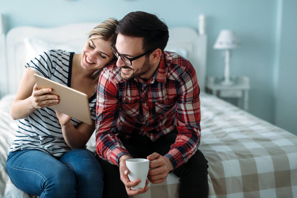 Young happy couple using digital tablet in bedroom - Photo, Image
