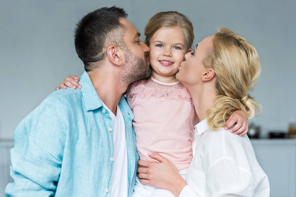 happy parents kissing adorable little daughter at home - Foto, afbeelding