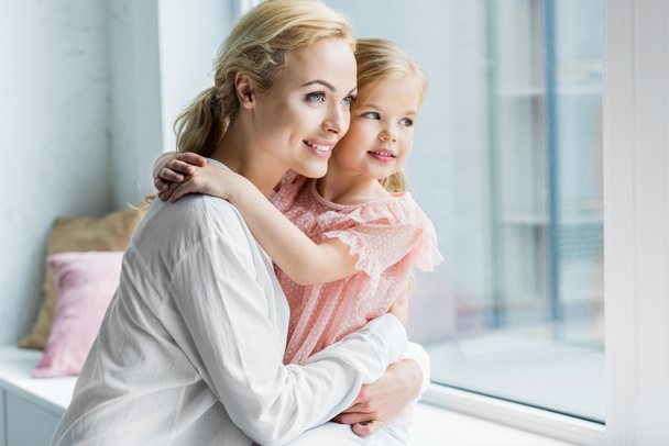 szép boldog anya és lánya, átölelve és látszó-on ablak - Fotó, kép