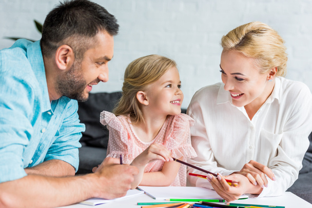 šťastní rodiče a roztomilá malá dcera kreslení s barevné tužky dohromady doma - Fotografie, Obrázek