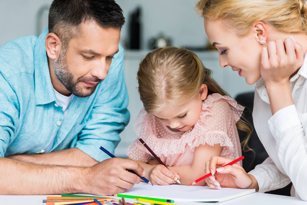 parents with cute little daughter drawing with colored pencils together at home - Photo, image