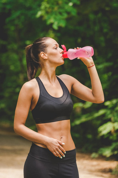 Portrait of athlete woman taking a break and drinking water in nature. - Photo, Image