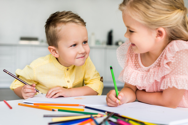 adorable kids smiling each other while drawing with colored pencils together - Photo, Image