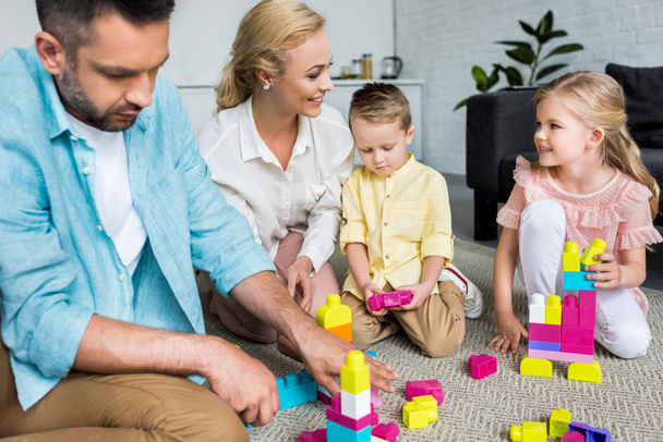 Счастливая семья с двумя детьми, играющая дома с разноцветными блоками
  - Фото, изображение