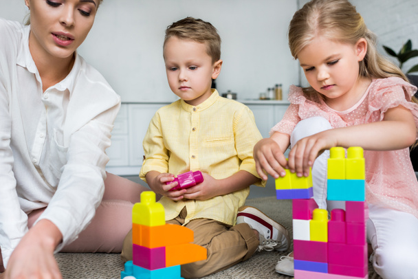 обрезанный снимок матери с милыми маленькими детьми, играющими с красочными блоками дома
 - Фото, изображение