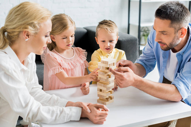 familia con dos niños construyendo torre de bloques de madera en casa
 - Foto, imagen