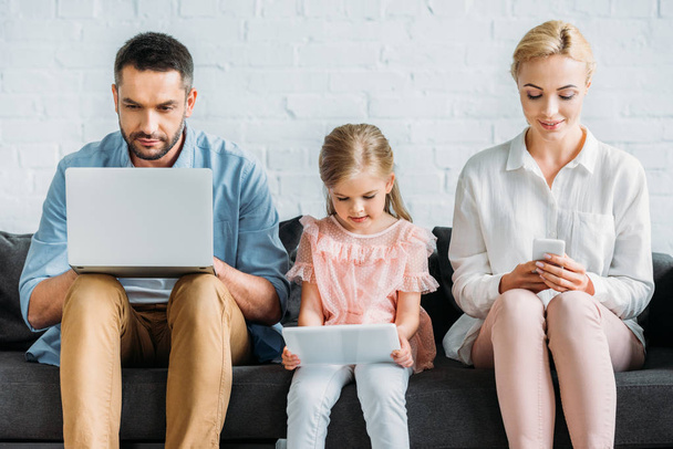 родители и милая маленькая дочь сидят на диване и с помощью цифровых устройств
  - Фото, изображение