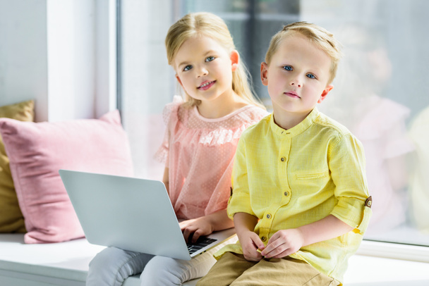 suloinen lapset käyttävät kannettavaa tietokonetta ja hymyilevät kameran kotona
 - Valokuva, kuva