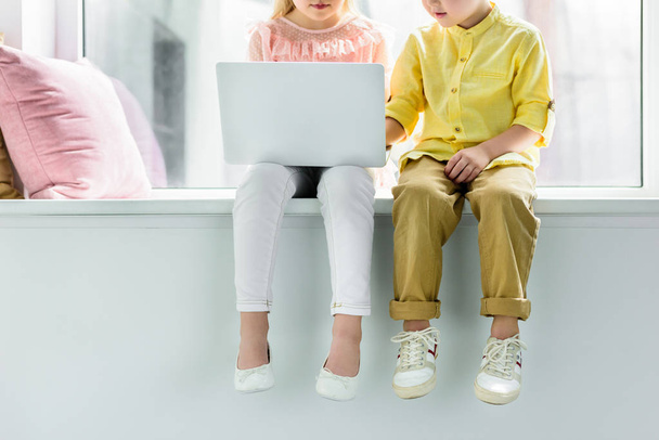 cropped shot of little kids sitting on windowsill and using laptop - Фото, изображение