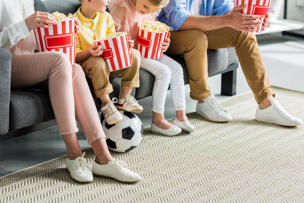 Schnappschuss von Familie, die Popcorn isst, während sie auf Sofa mit Fußballball sitzt - Foto, Bild
