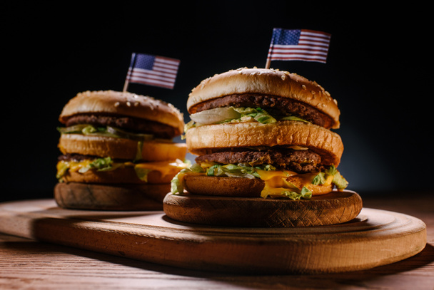 primo piano di deliziosi hamburger con spilli bandiera USA su tagliere in legno su nero
 - Foto, immagini