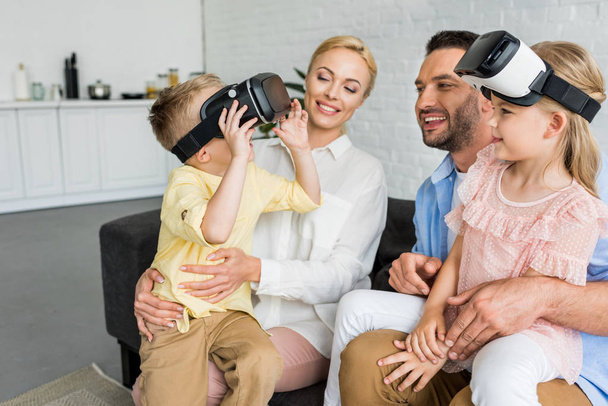 happy parents looking at cute little kids using virtual reality headsets at home - Foto, immagini