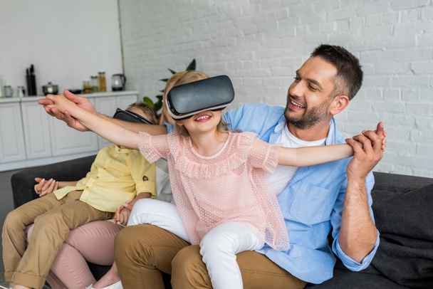 happy parents playing with kids using virtual reality headsets at home - Fotó, kép