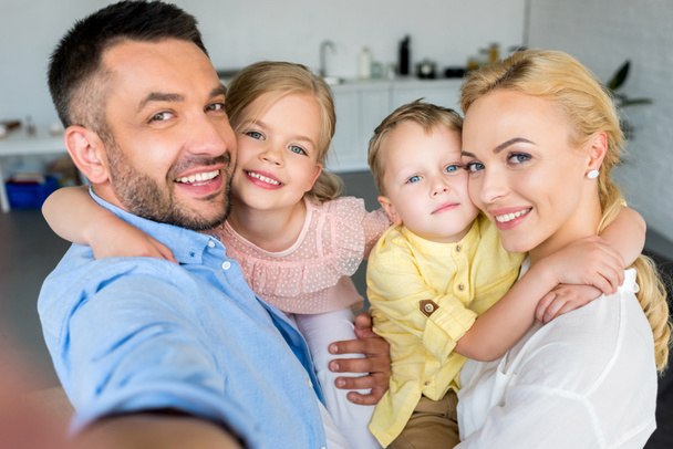 Счастливая семья с двумя детьми обнимается и улыбается на камеру дома
 - Фото, изображение