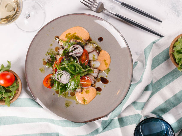 Свіжий салат з восьминогами, помідорами, руколою та цибулею, подається з соусом на тарілці
 - Фото, зображення