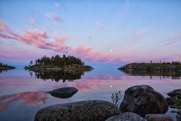 Spectaculaire blauwe uur landschap net na zonsondergang. Roze wolken en volle maan worden weerspiegeld in het meer van Ladoga, gelegen in Karelië, ten noorden van Rusland. Selectieve aandacht. - Foto, afbeelding
