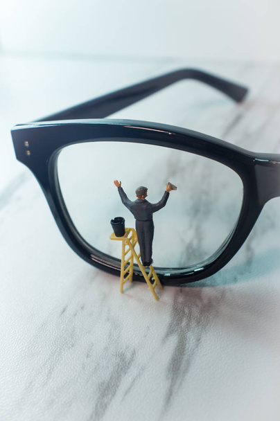 Оптические очки чистятся крошечной фигуркой, символизирующей ясное зрение - Фото, изображение