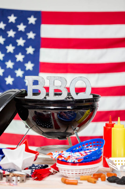 Metalen BBQ-teken op kleine ronde houtskool barbecue met 4 juli-decoraties. - Foto, afbeelding