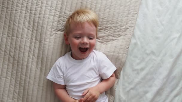 Μαμά χαϊδεύει το αγόρι ξαπλωμένη στο κρεβάτι που κοιτάζει απευθείας στην κάμερα και να γελάει δυνατά - Πλάνα, βίντεο
