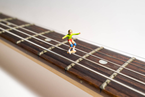 Miniature skateboarding figures grind down guitar strings in macro closeup - Photo, Image