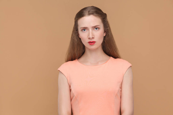 sad woman with makeup and long hair in pink dress looking at camera on brown background - Photo, Image
