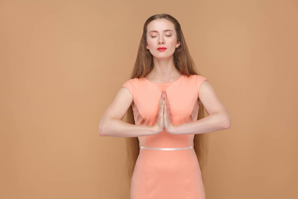 beautiful woman in pink dress keeping eyes closed and doing yoga pose on brown background, Spiritual practice concept  - Foto, Imagem