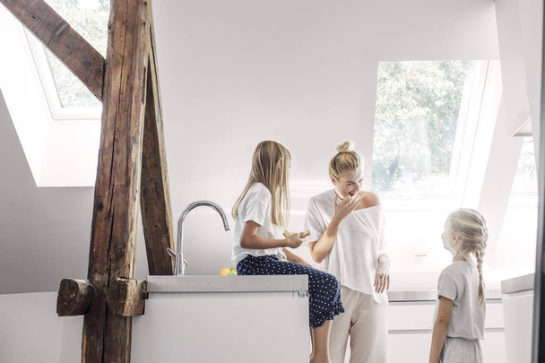Pretty Caucasian smiling woman enjoying morning meal in kitchen with her cute daughters. - Fotografie, Obrázek