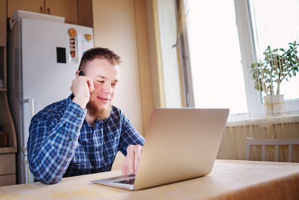 Jonge zakenman kijkend naar een grafiek die is liggend op zijn laptop met diepe concentratie terwijl op zijn telefoon op zijn Bureau. - Foto, afbeelding