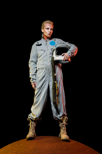 attractive female cosmonaut in spacesuit holding helmet and standing on planet - Photo, Image