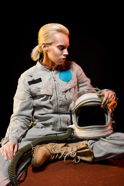 beautiful female cosmonaut in spacesuit and helmet sitting on planet - Photo, Image