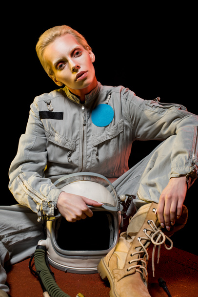 fashionable female astronaut in spacesuit and helmet sitting on planet - Photo, Image