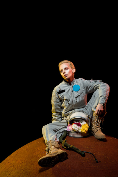 beautiful astronaut in spacesuit with flowers in helmet sitting on planet  - Foto, immagini