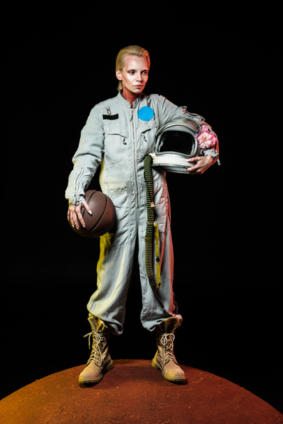cosmonauta en traje espacial sosteniendo pelota de baloncesto y casco con flor mientras está de pie en el planeta rojo
  - Foto, imagen