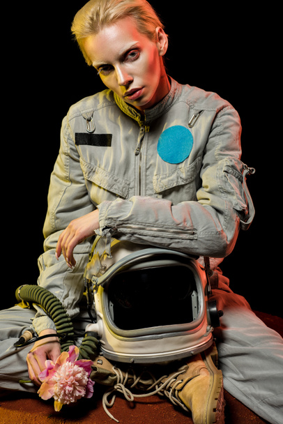 attractive young astronaut in spacesuit with helmet and peony sitting on planet - Photo, Image