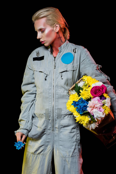 vonzó női űrhajós pózol Szkafander és a színes virágok papírzacskóban, elszigetelt fekete - Fotó, kép
