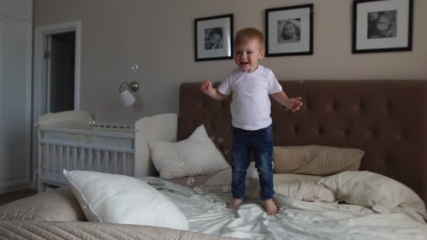 Jumping off of happiness on the bed looking at flying soap bubbles - Footage, Video