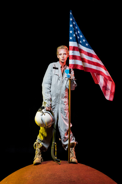 attractive female astronaut in spacesuit holding helmet and american flag on planet  - Photo, Image