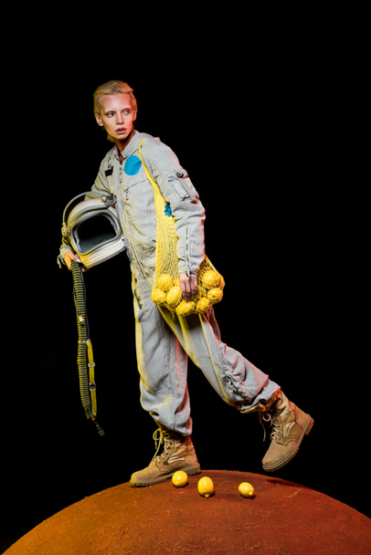ελκυστική γυναίκα αστροναύτης στη διαστημική στολή κρατώντας το κράνος και τα λεμόνια στον κόκκινο πλανήτη  - Φωτογραφία, εικόνα