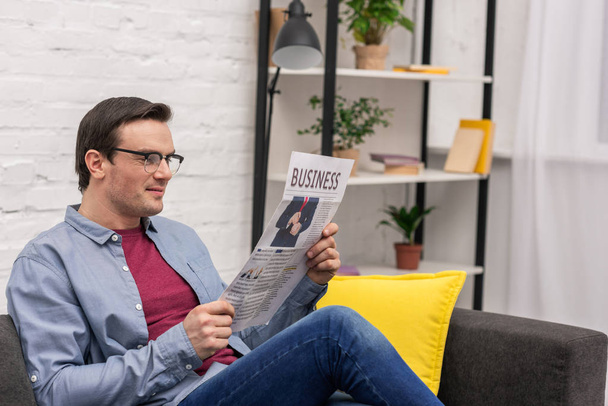 handsome adult man reading newspaper while sitting on couch at home - Fotoğraf, Görsel