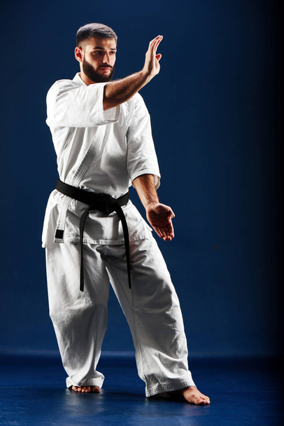 barefoot man in white kimono with black belt standing in fighting stance on dark background - Fotografie, Obrázek