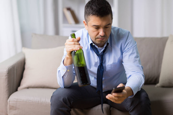 man with smartphone and bottle of alcohol at home - Φωτογραφία, εικόνα